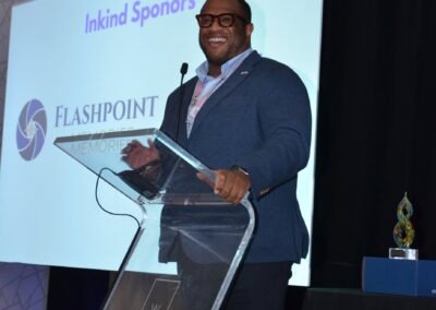 A speaker at the podium beside a sponsor recognition slide at an Orlando event