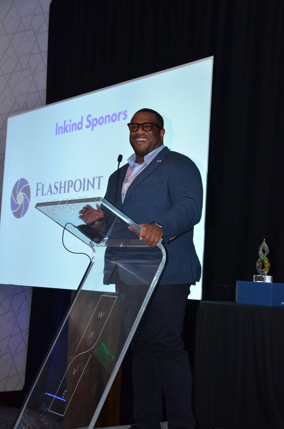 A speaker at the podium beside a sponsor recognition slide at an Orlando event