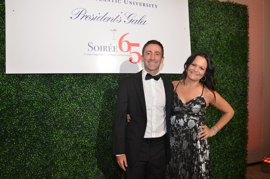 A couple in black tie photographed at a branded gala backdrop
