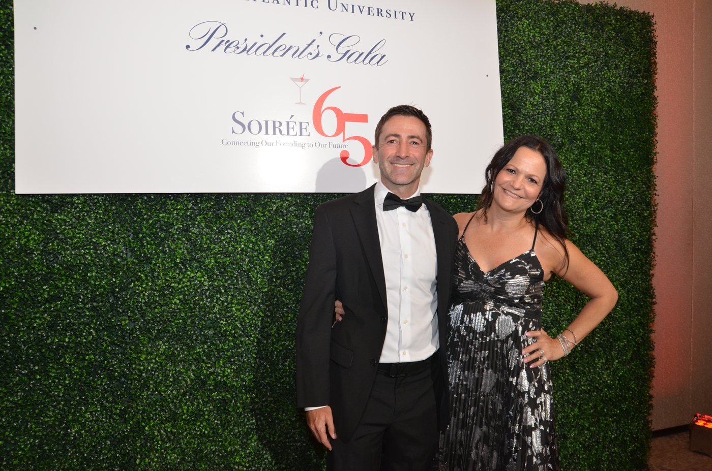 A couple in black tie photographed at a branded gala backdrop at The Boca Raton