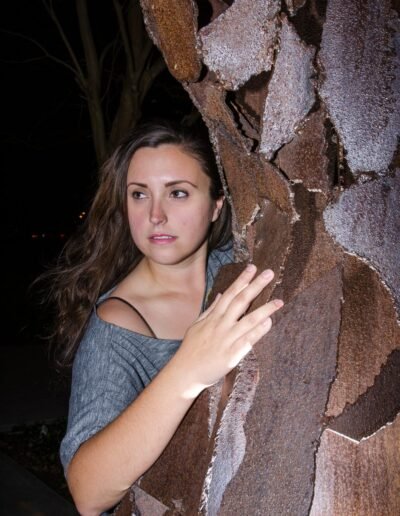 Environmental portrait of a woman beside a textured tree at night