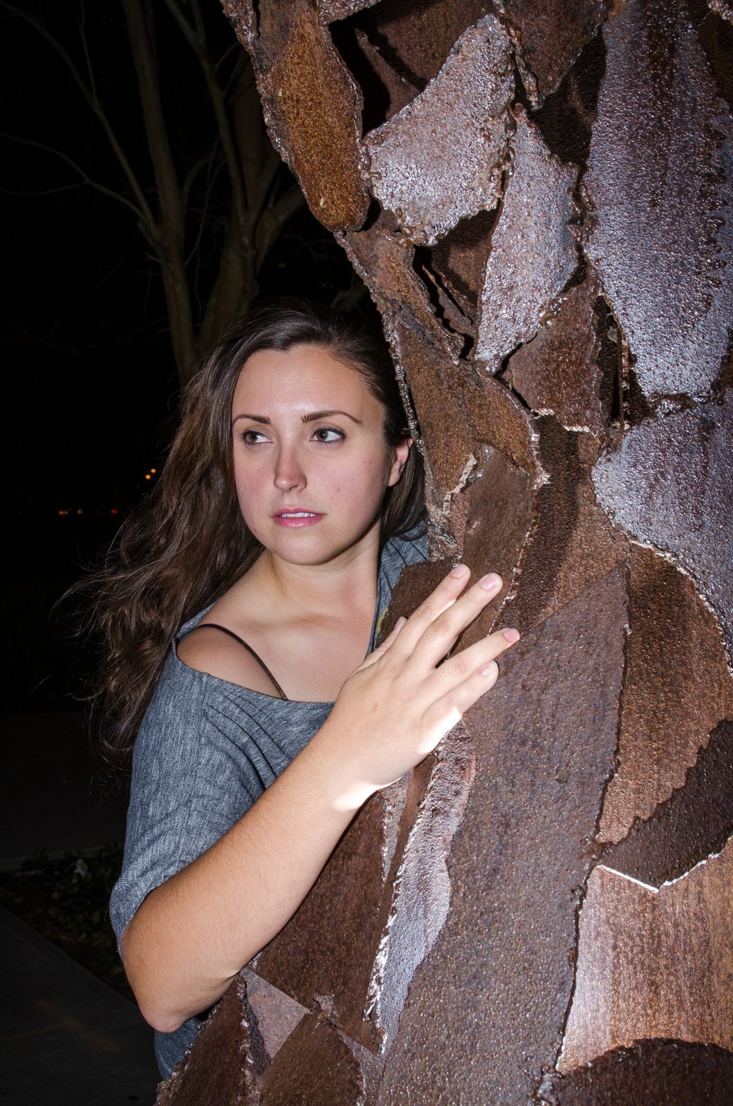 Environmental portrait of a woman beside a textured tree at night