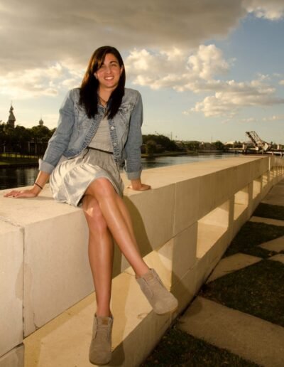 Portrait of a woman seated on a riverside wall at dusk
