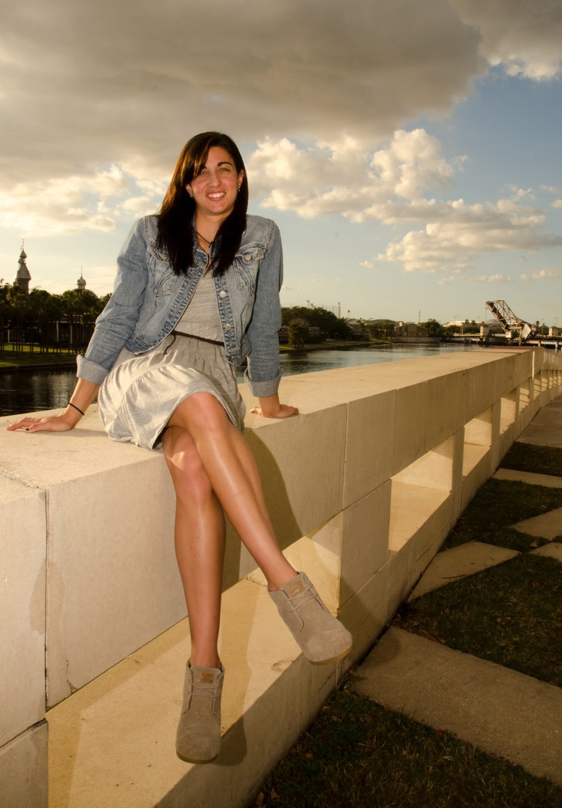 Portrait of a woman seated on a riverside wall at dusk